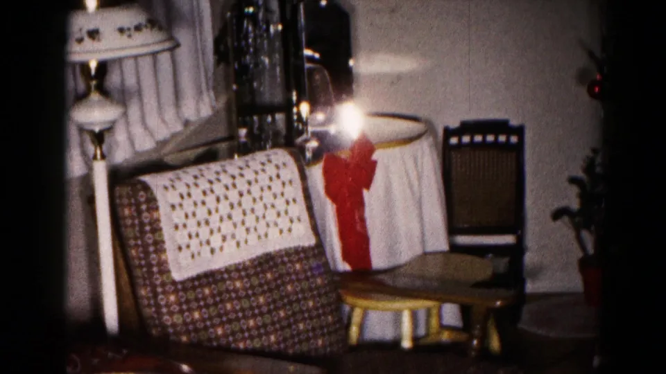 1959 Hagerstown home interior showing a patterned sofa with crocheted throw, floor lamp, bow-trimmed table, chair, curtains, and small potted plant.