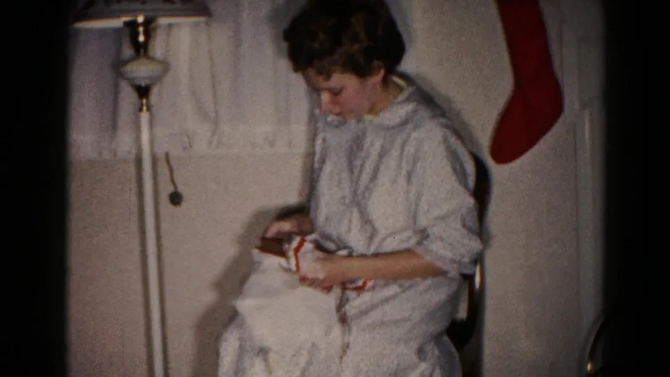 A side view shows the woman in a light nightgown handling the Christmas present near a floor lamp in the 1959 home interior.