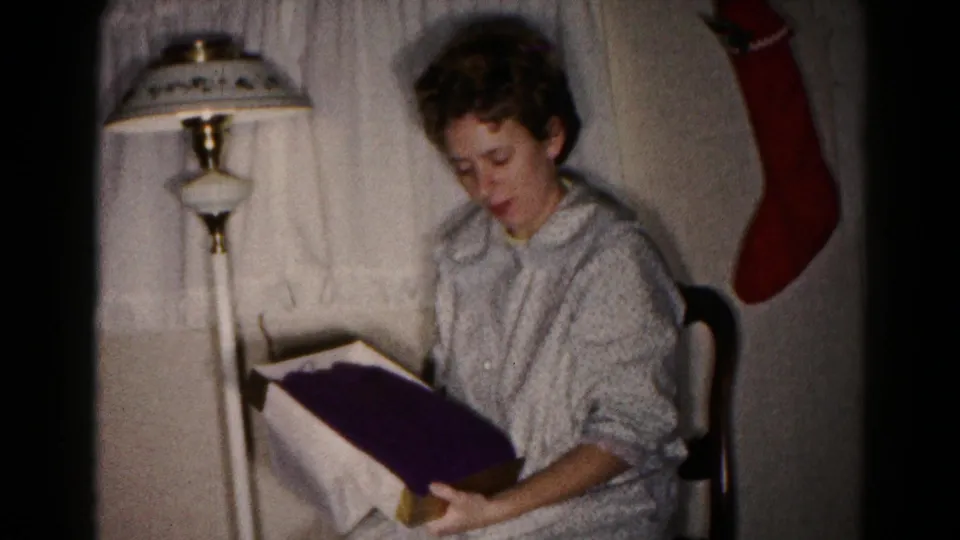 The opened present reveals dark fabric as the seated woman holds the box in the Hagerstown Christmas home-movie scene.