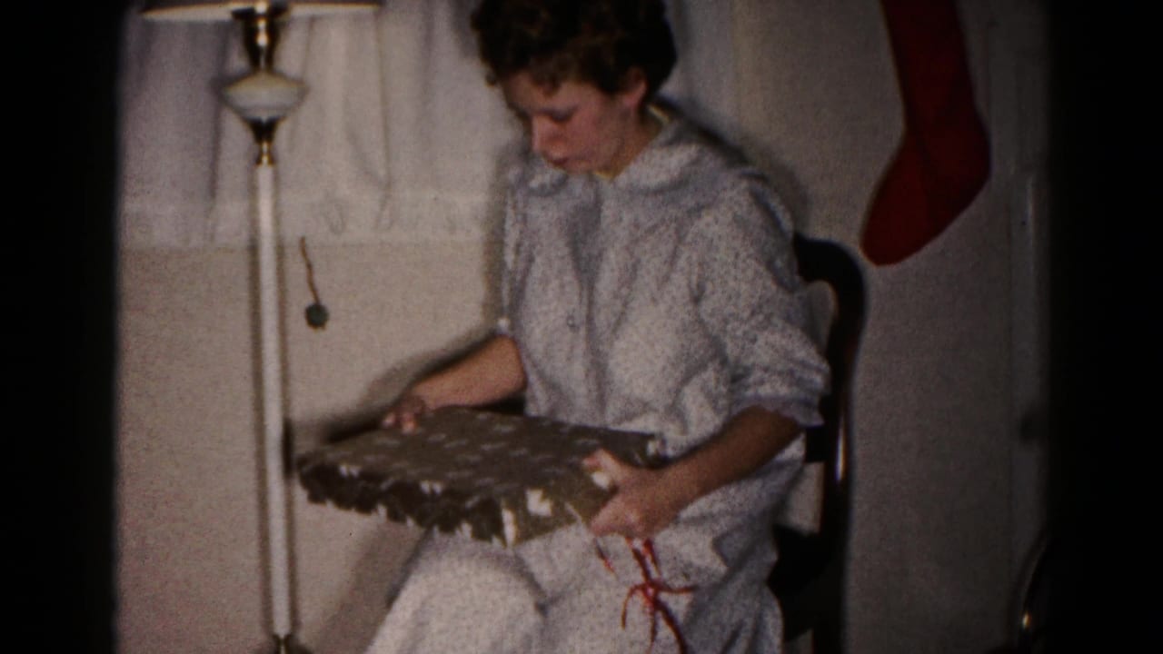 Woman holds a partly opened gift box while seated near a hanging red stocking.