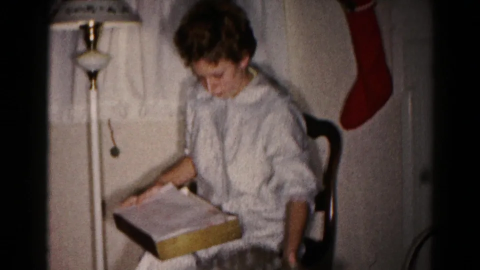 The woman looks into the opened gift box during a 1959 Christmas home-movie moment inside a private Hagerstown residence.
