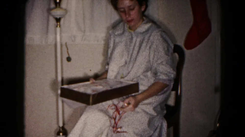 In the closing frame, the young woman looks down at the gift box on her lap in a 1959 Hagerstown Christmas interior.