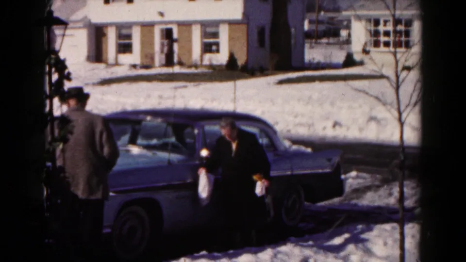 A snowy Hagerstown street scene shows a man in a hat and a woman near a mid-century sedan, with houses behind them.