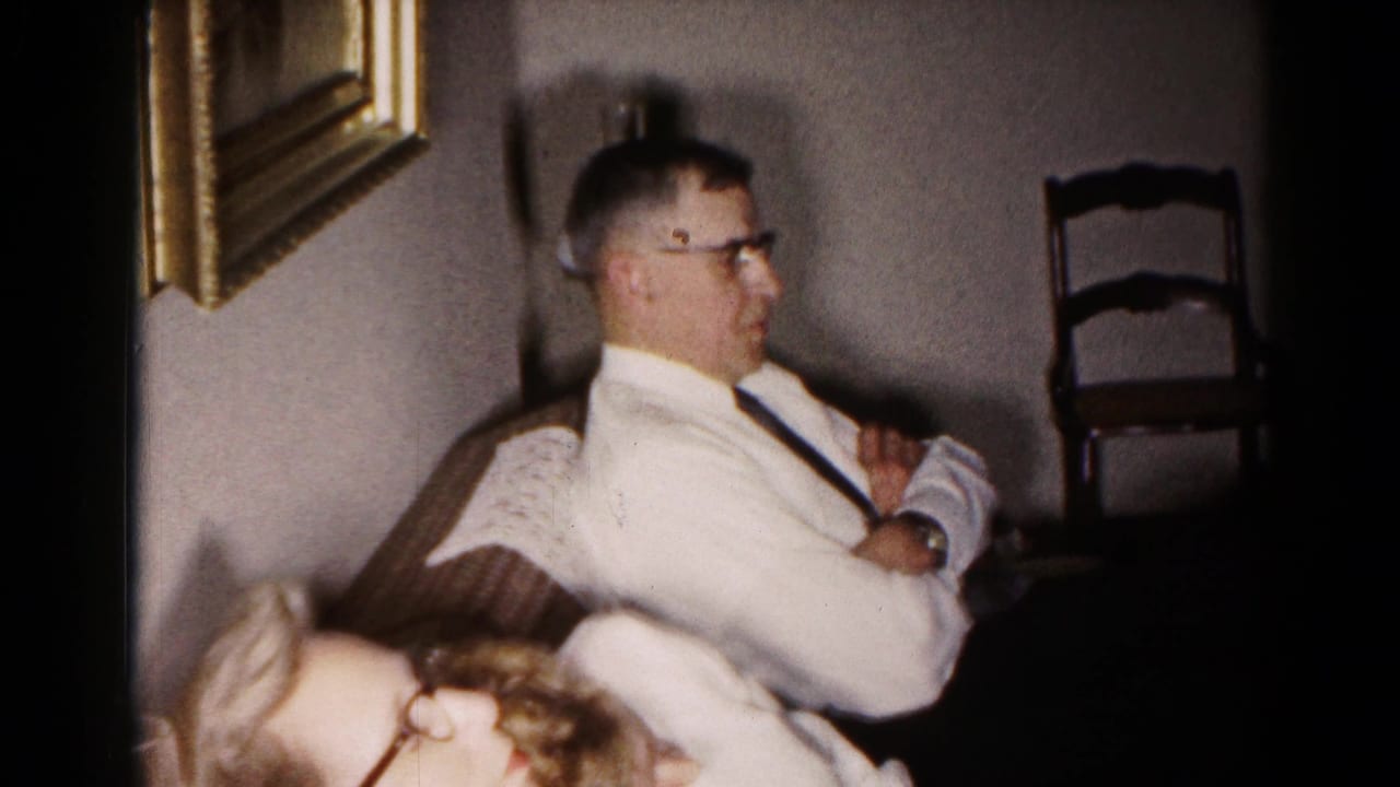 1959 Hagerstown home-movie frame showing a seated man in profile and a woman in glasses leaning through the foreground of a private interior.