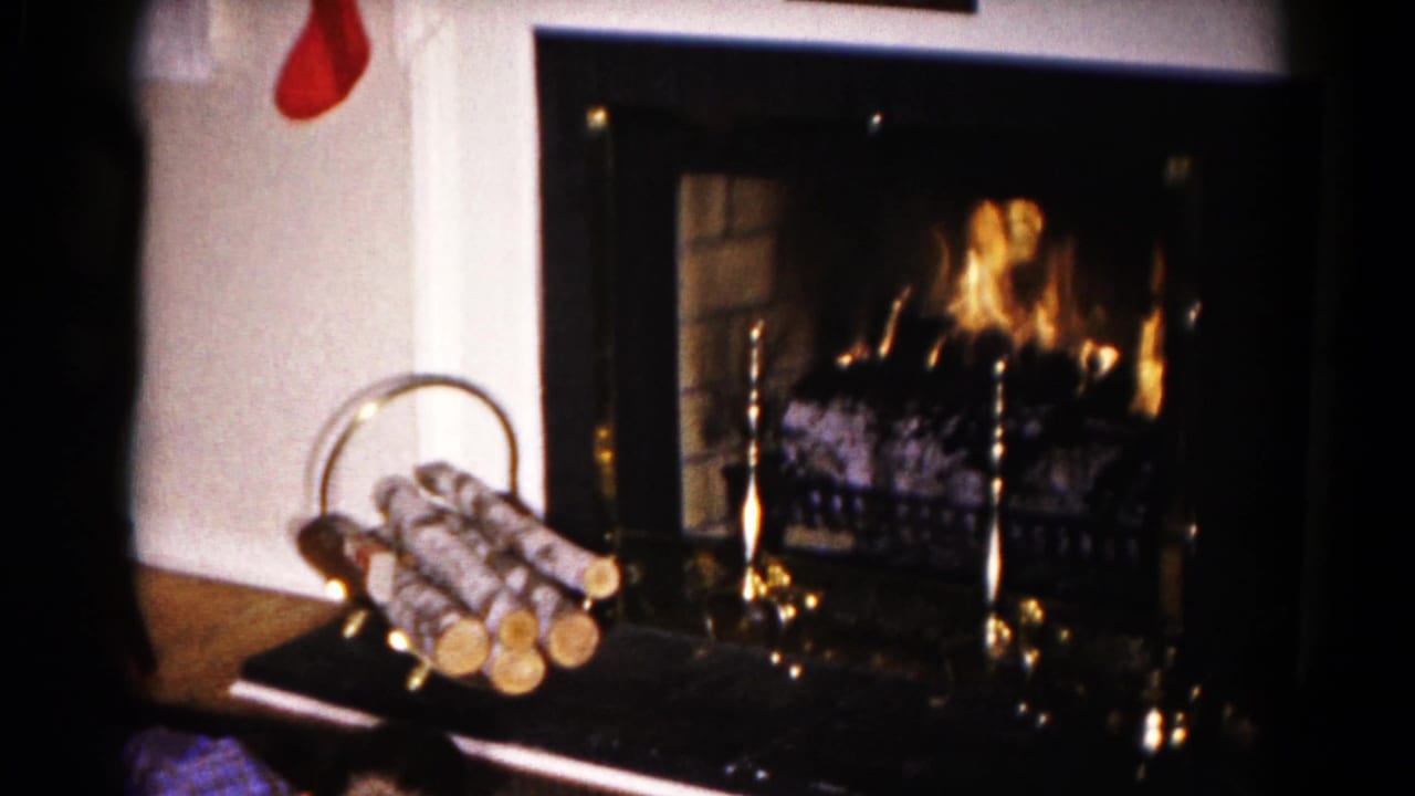 Burning fireplace with white mantel, red stocking edge, brass tools, and a basket of logs.