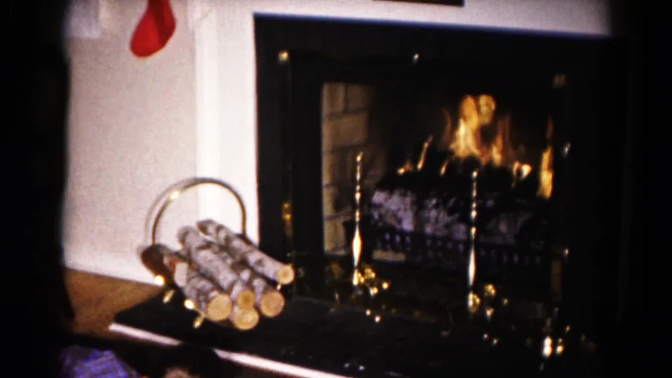 1959 Hagerstown home-movie frame showing a decorated Christmas fireplace with logs, brass tools, and a red stocking partly visible.