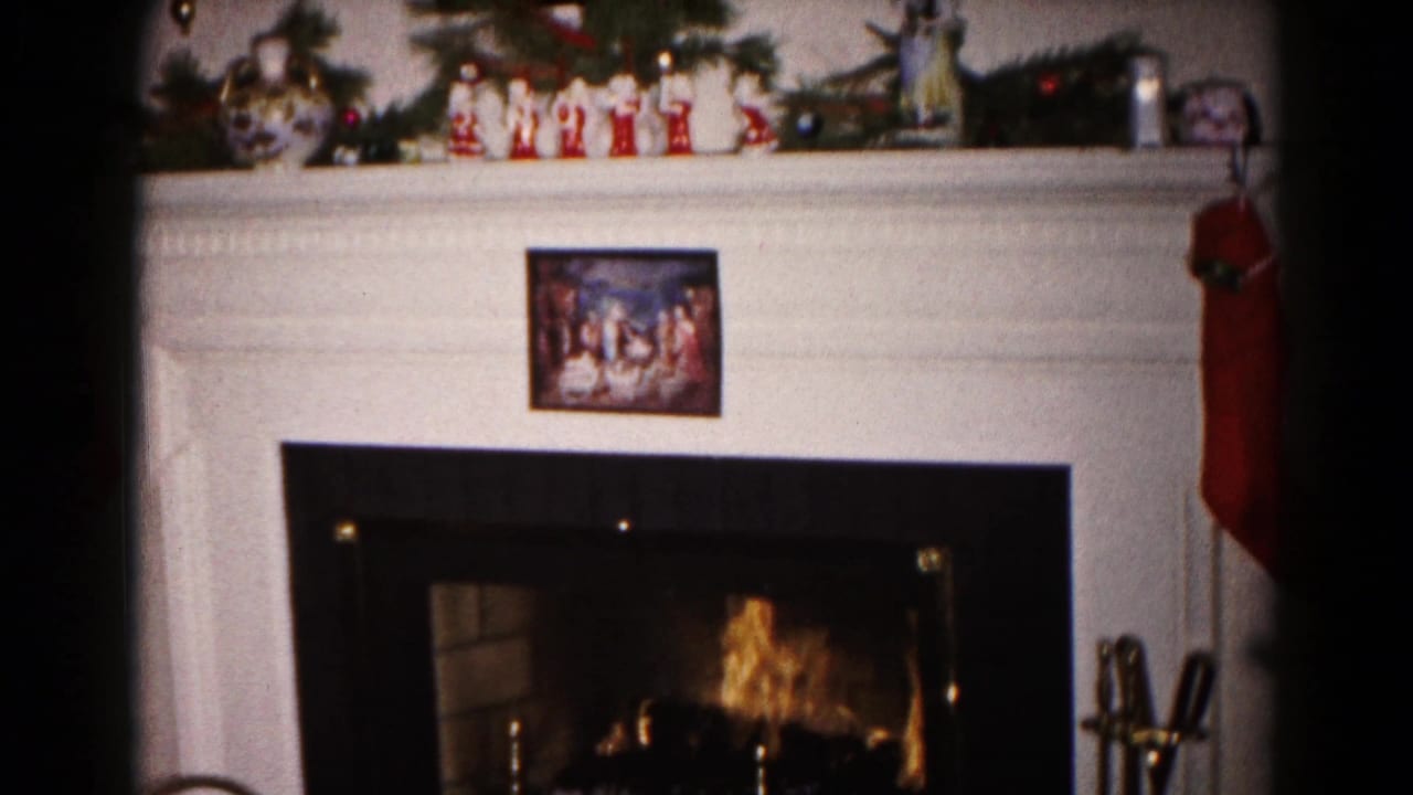 1959 Hagerstown Christmas interior showing mantel greenery, small figurines, red stocking, brass tools, and a glowing fireplace.