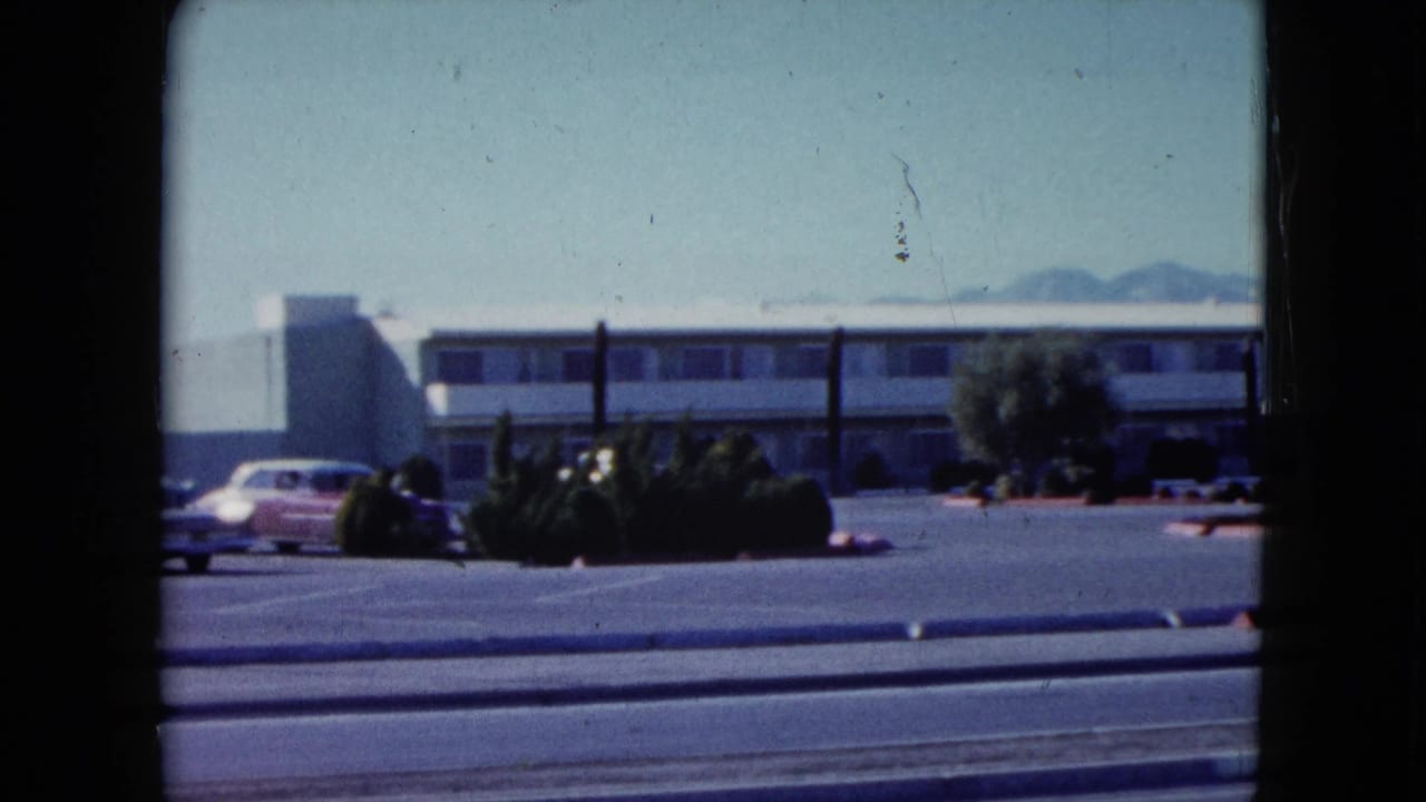 Motel building and parked cars viewed across a road from a moving vehicle.