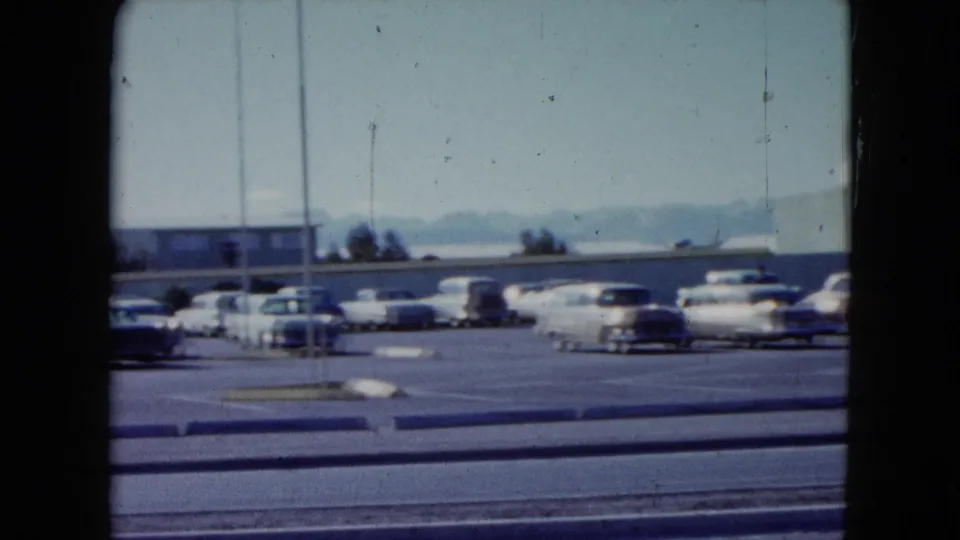 1959 Nevada motel-area parking lot with rows of classic cars, roadside lanes, a light pole, distant mountains, and a clear sky.