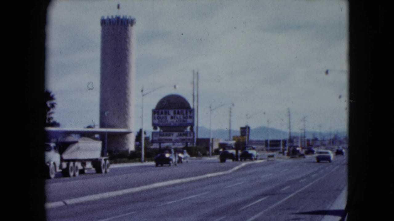 1959 Nevada 8mm frame showing classic cars on a broad road beside a tan cylindrical tower, palm trees, and a Pearl Bailey sign.