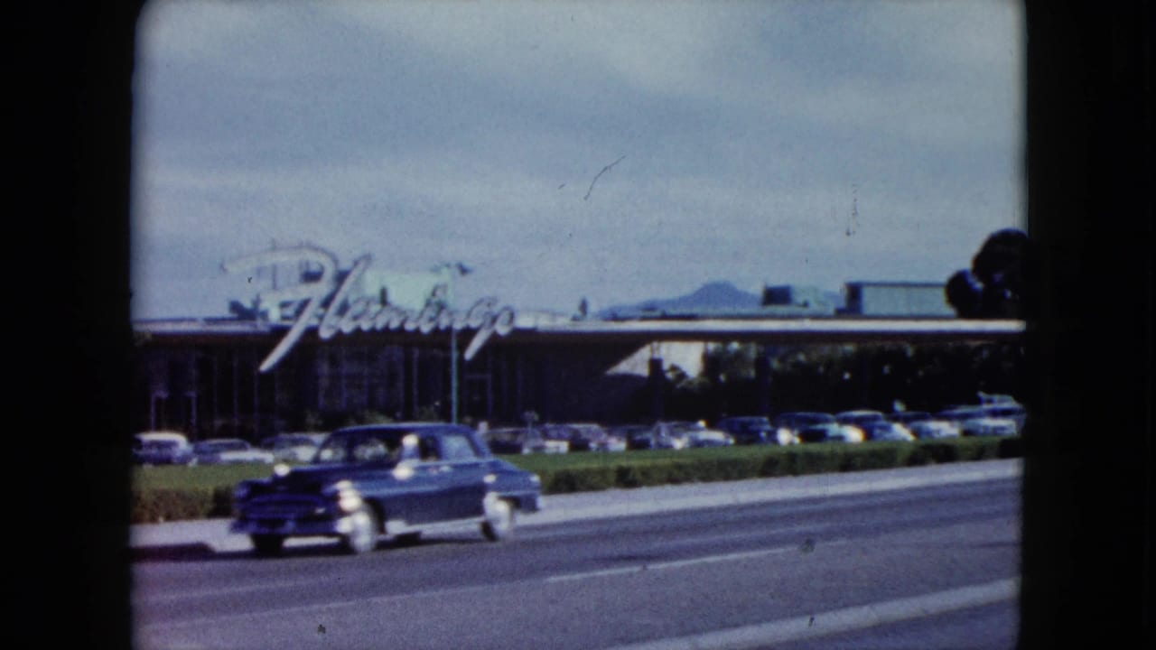 1959 Nevada 8mm frame showing a blue classic car passing near the camera, with the Flamingo sign and roadside parking behind.
