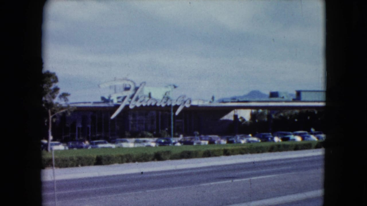 1959 Nevada 8mm frame showing the Flamingo sign, a long roadside building, vintage parked cars, and a broad road in front.