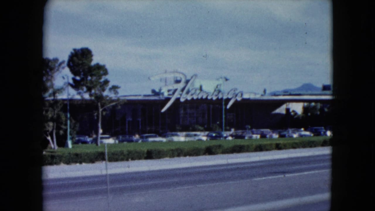 1959 8mm view of the Flamingo Hotel in Las Vegas, seen across a roadway with landscaping, parked cars, and soft home-movie color.