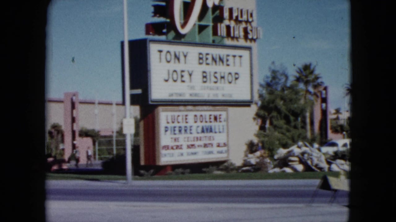 1959 Nevada frame showing a wider roadside view of the Dunes sign, marquee, cars, palm trees, and hotel-area landscaping.
