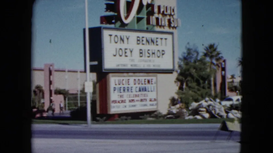 1959 Nevada frame showing a wider roadside view of the Dunes sign, marquee, cars, palm trees, and hotel-area landscaping.