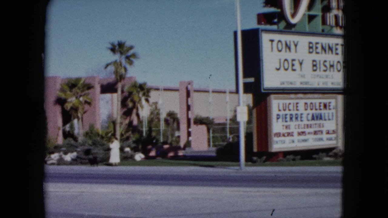 Marquee edge, palm trees, sidewalk landscaping, and low commercial building across the street.