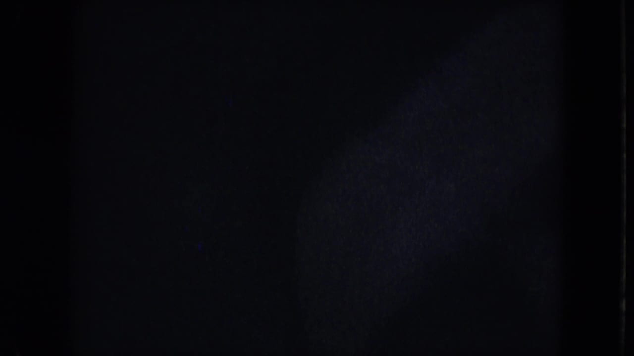 Dark opening frame from the 8mm scan, with only faint film texture and edge exposure visible before the street scene appears.