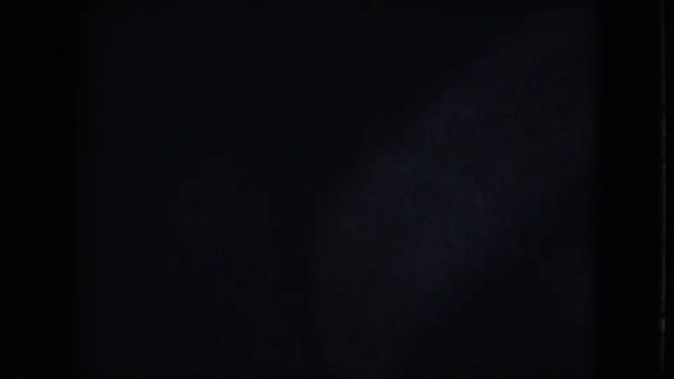 Dark opening frame from the 8mm scan, with only faint film texture and edge exposure visible before the street scene appears.