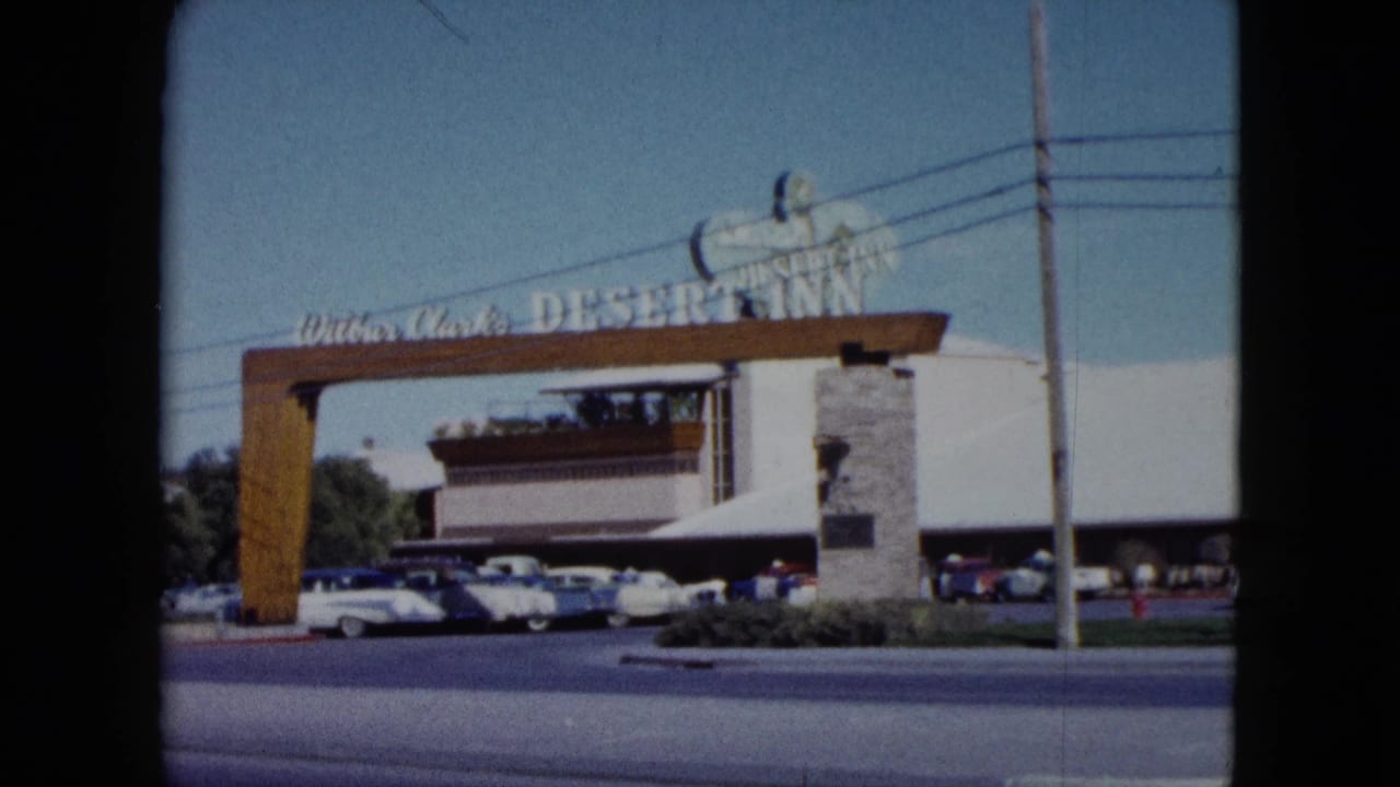 1959 Nevada frame of the Desert Inn entrance, with the arched sign, resort building, parked cars, and overhead utility wires visible.