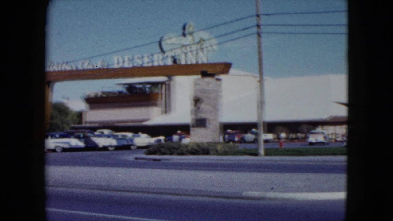1959 Nevada roadside view of the Desert Inn entrance, showing the sign partly across the frame, parked cars, resort frontage, and street lanes.