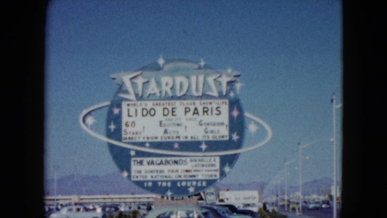 Large Stardust Hotel sign advertising Lido de Paris in Nevada, with cars, roadside poles, blue sky, and distant mountains.