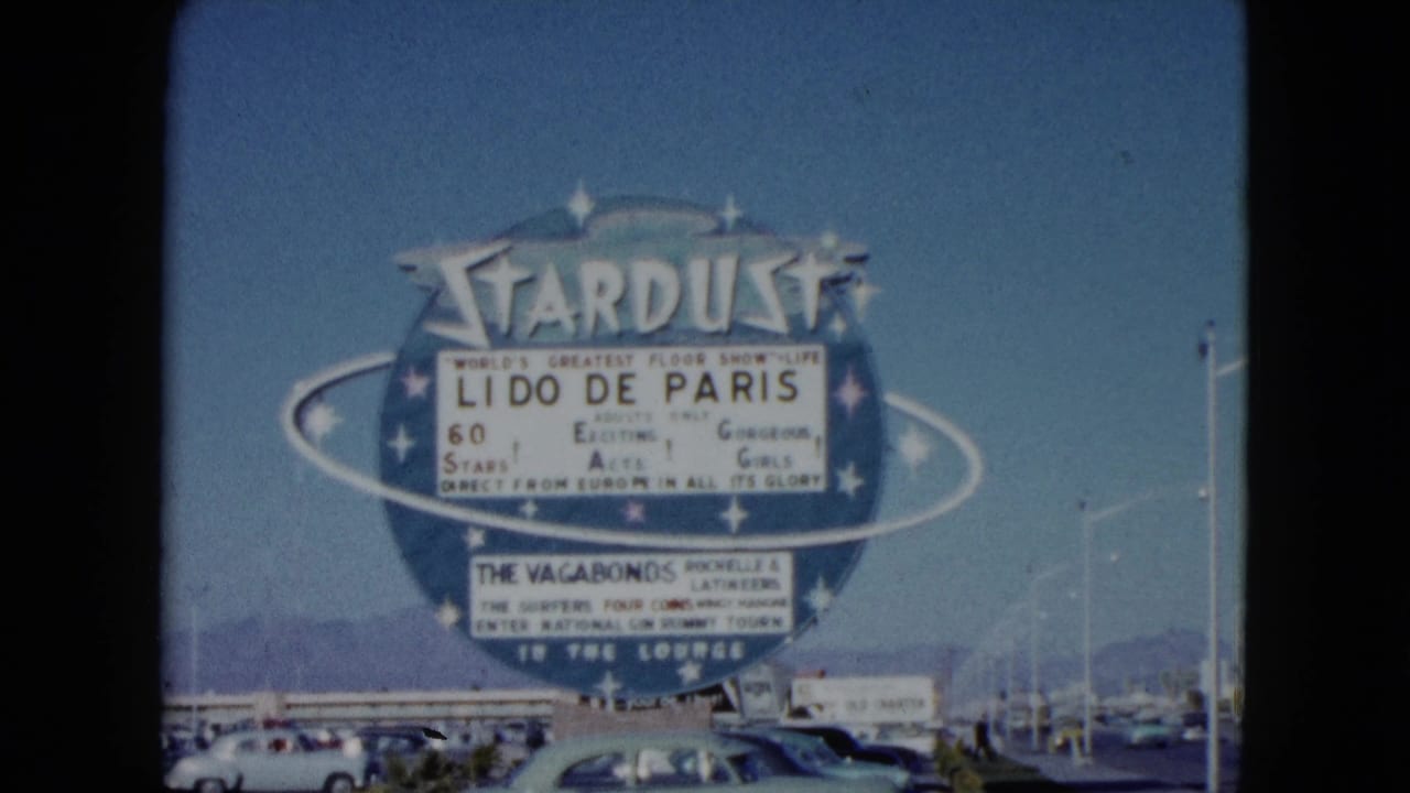 1959 Nevada home-movie frame of the Stardust sign advertising Lido de Paris above parked classic cars and distant mountains.