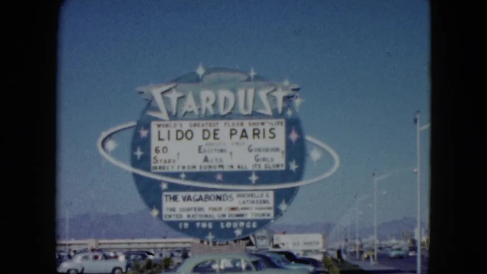 1959 Nevada home-movie frame of the Stardust sign advertising Lido de Paris above parked classic cars and distant mountains.