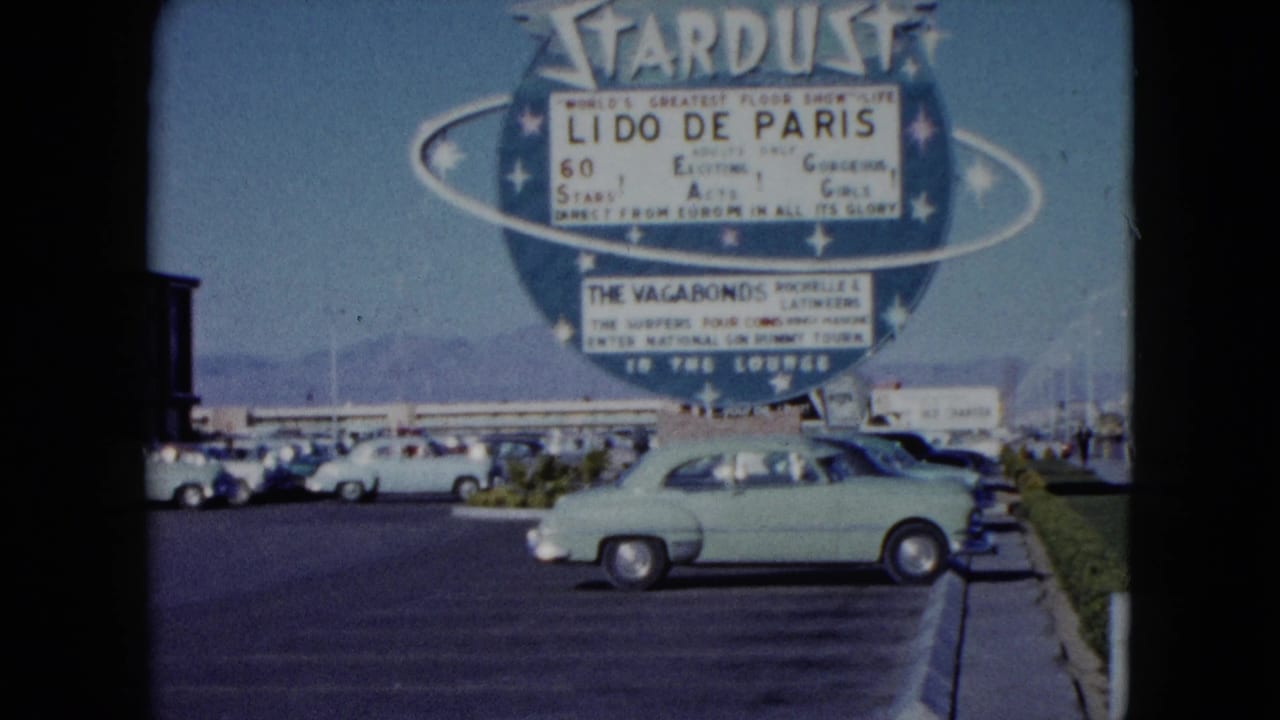 1959 Nevada home-movie view of the Stardust marquee, parked mid-century cars, and a light green sedan near the curb.