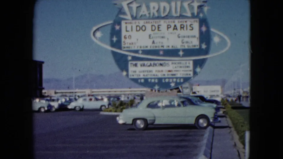 1959 Nevada home-movie view of the Stardust marquee, parked mid-century cars, and a light green sedan near the curb.
