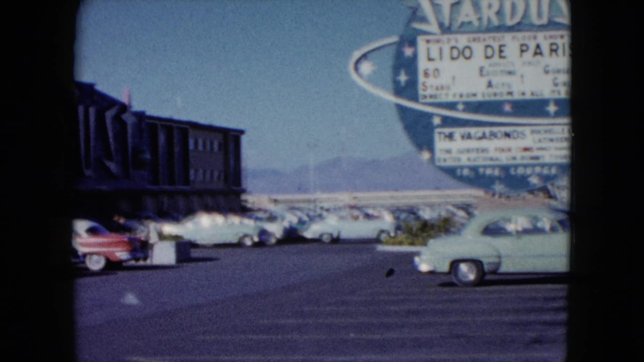 1959 Nevada frame with the Stardust sign partly cropped, classic cars in the lot, and a dark roadside building at left.