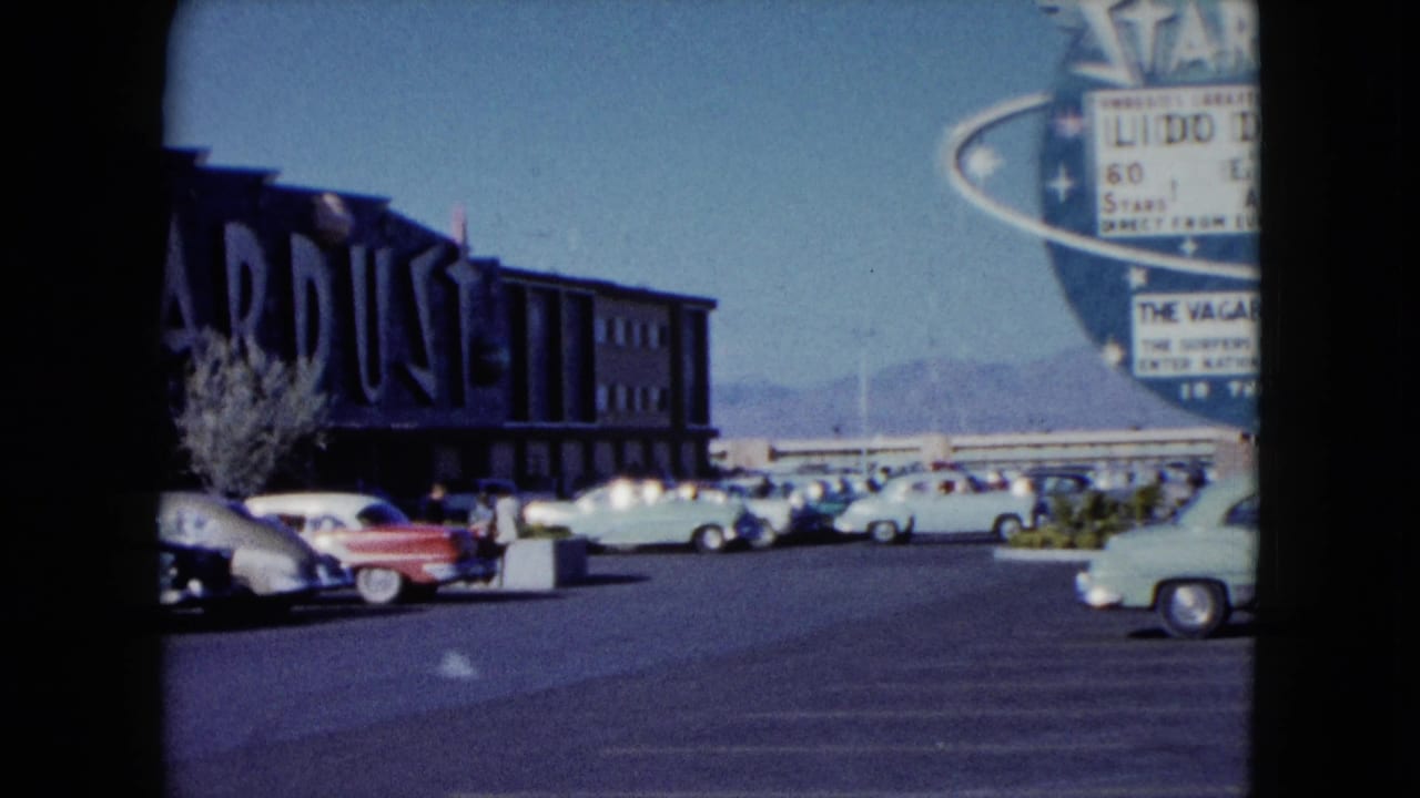 1959 Nevada 8mm frame showing the Stardust building area, marquee edge, parked cars, clear sky, and distant mountains.