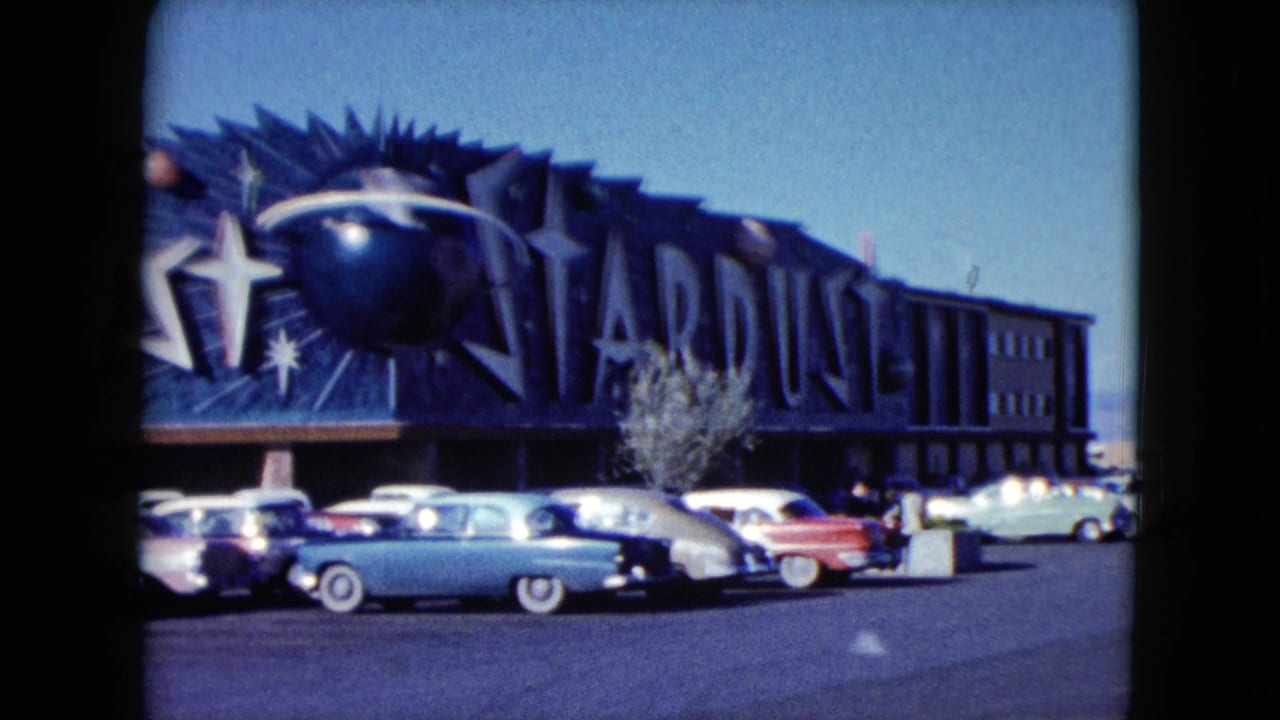 1959 Nevada 8mm frame showing a closer view of the Stardust sign, star graphics, pastel cars, and sunlit parking lot.