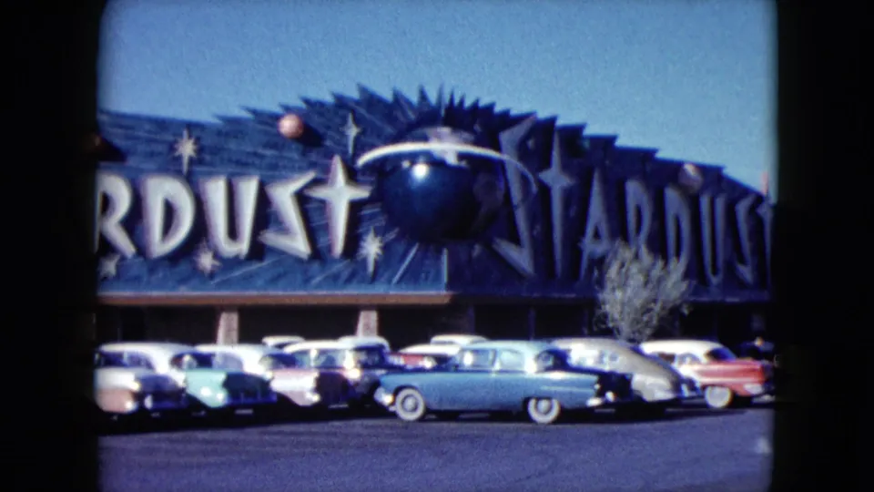 1959 Nevada home-movie frame showing the Stardust sign with star and planet graphics above parked classic cars.