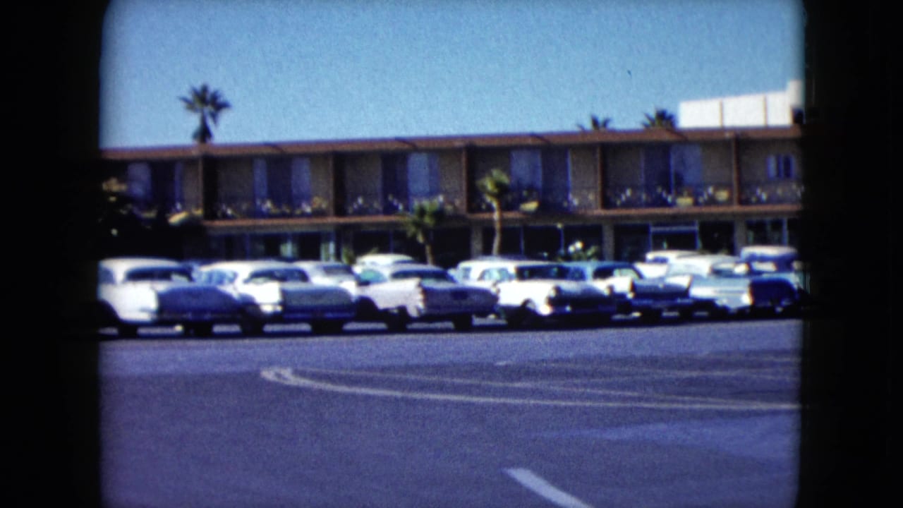 1959 Nevada home-movie frame showing parked cars outside a low-rise motel under a clear blue sky.