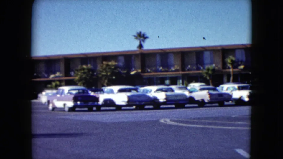 1959 Nevada motel exterior with classic cars across the parking lot, framed by 8mm film gate edges.