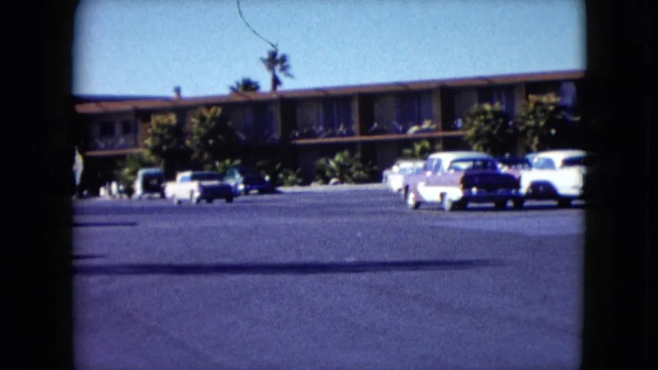 1959 Nevada home-movie frame showing a wider view of the motel parking area and parked cars.