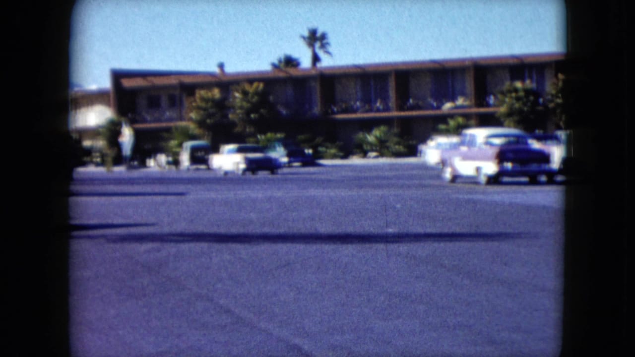 Low-rise motel across a parking lot with classic cars and palm trees.