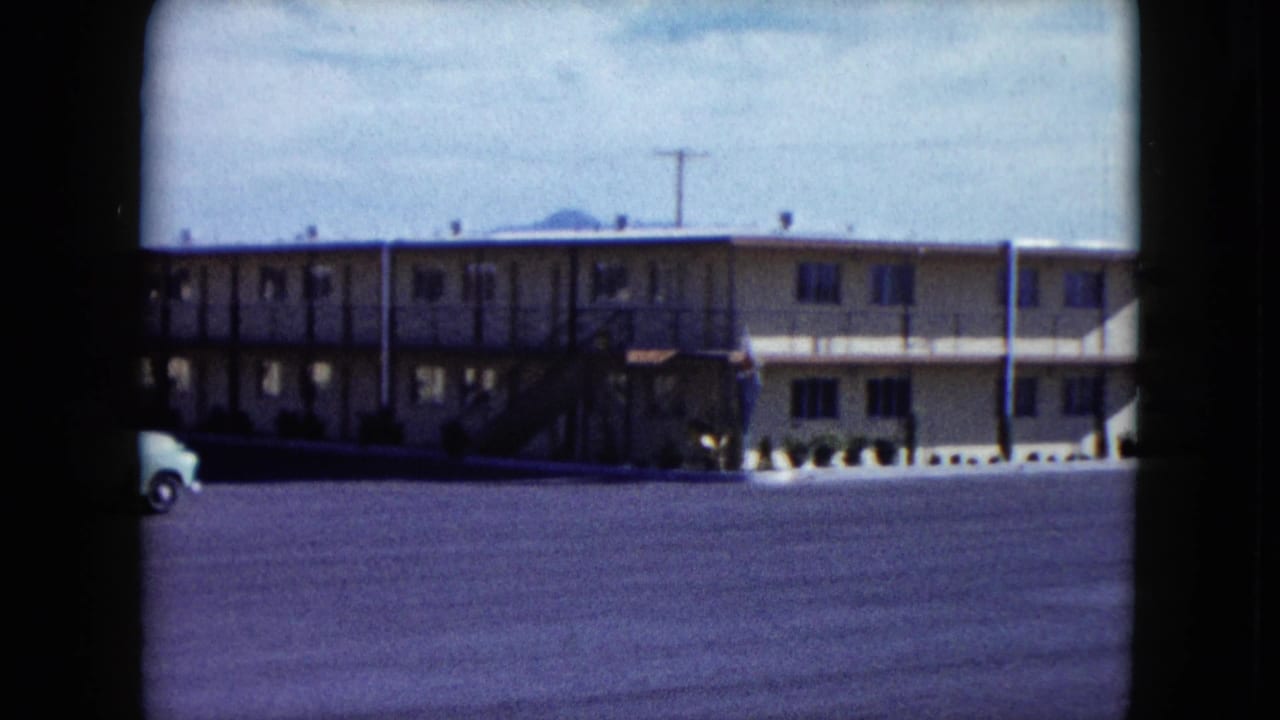 Motel exterior and mostly empty parking lot, with a vehicle partly entering at left.