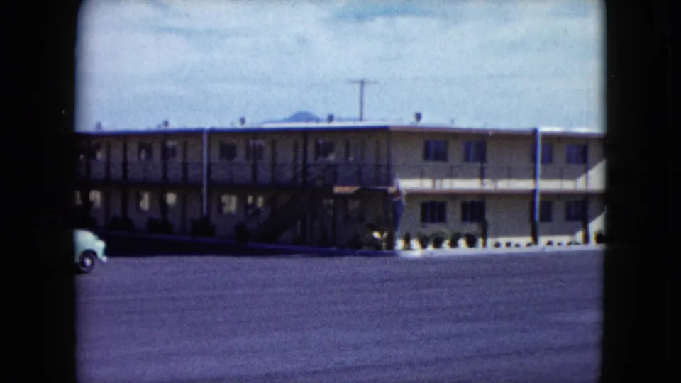 1959 Nevada motel exterior with a broad asphalt lot and a light-colored vehicle partly visible along the left edge of the frame.