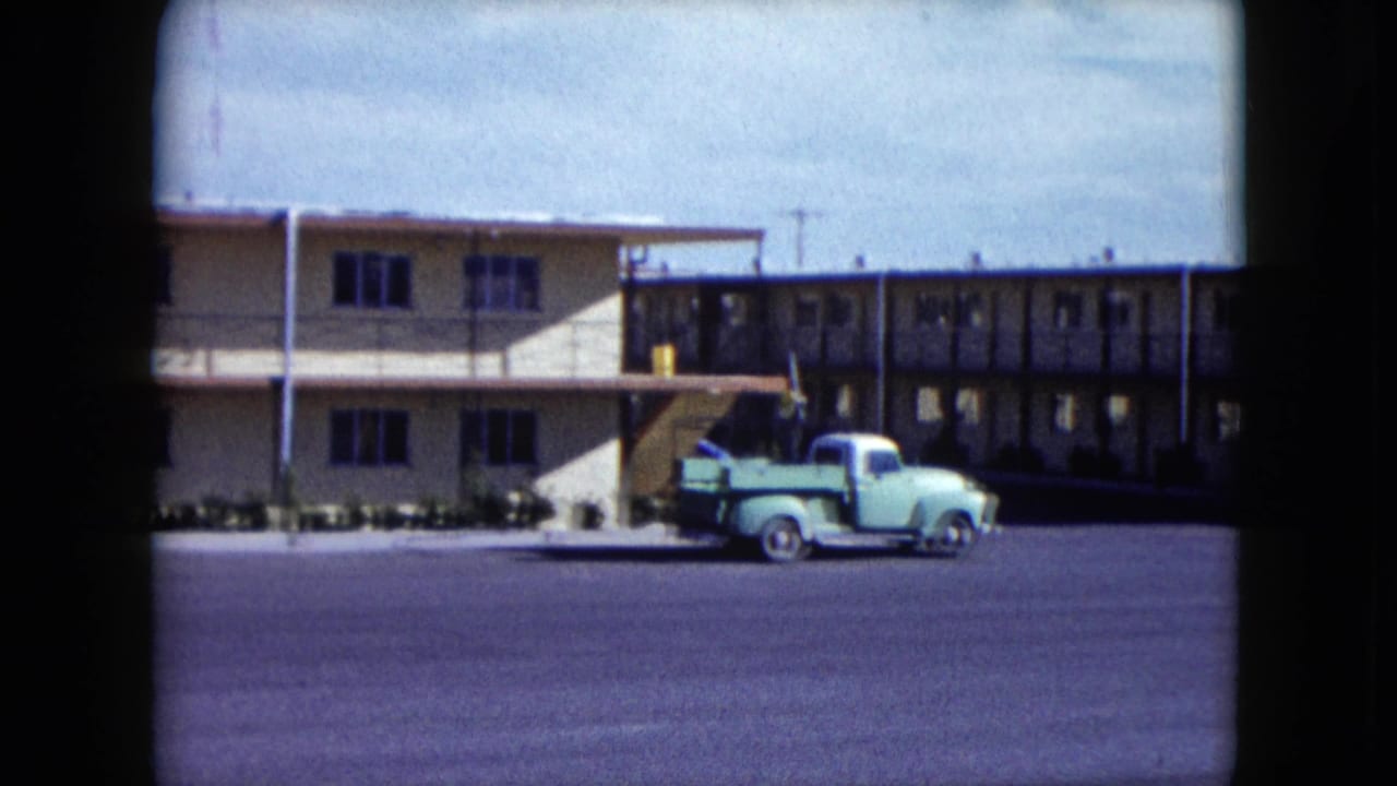 1959 Nevada home-movie frame showing a light green pickup beside a tan two-story roadside building with exterior walkways.