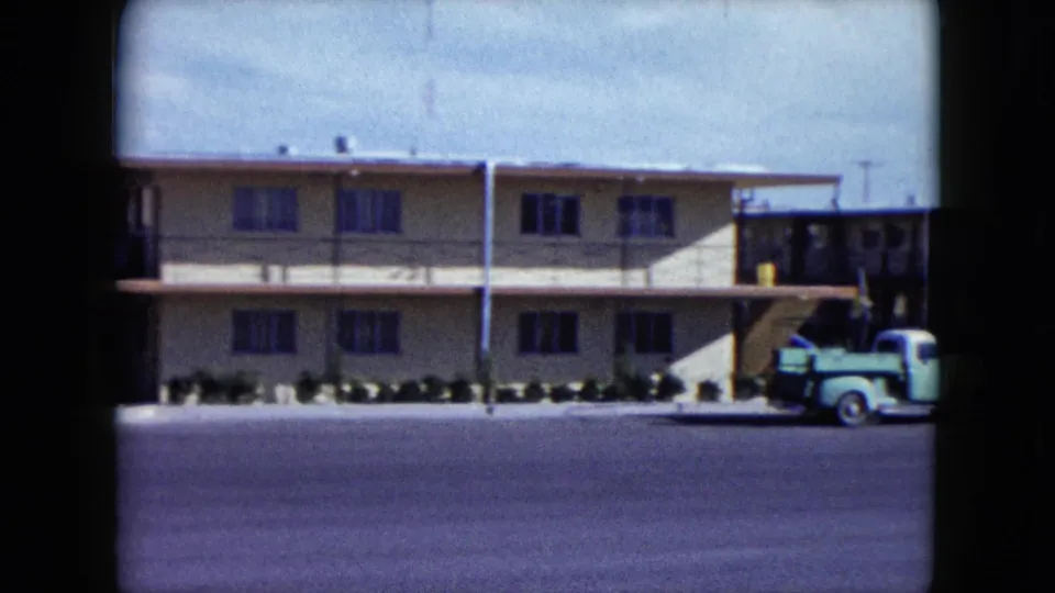 The camera holds on a Nevada roadside building facade with a vintage green pickup parked near an exterior stair or entry area.