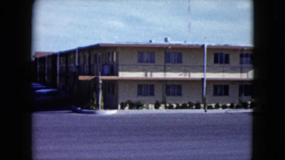1959 Nevada frame showing more of the tan two-story building, with exterior walkways, window rows, and a broad empty paved area.
