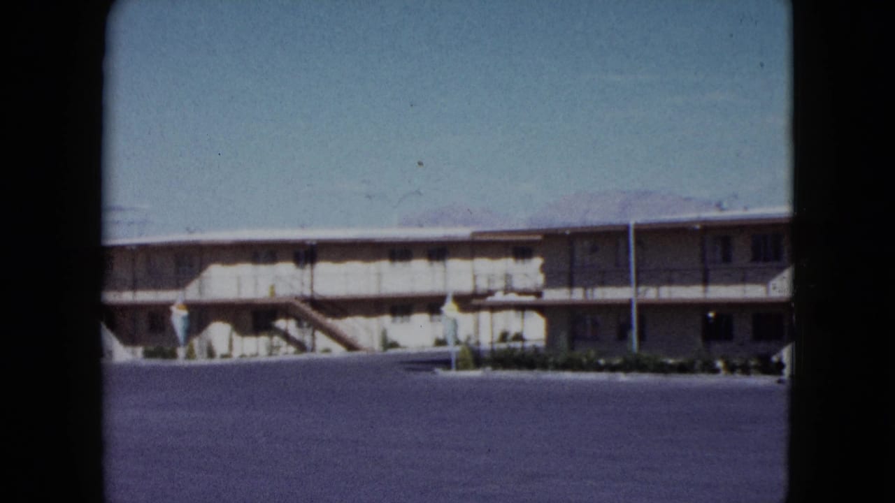 Motel facade with exterior stairs and open paved lot in front.