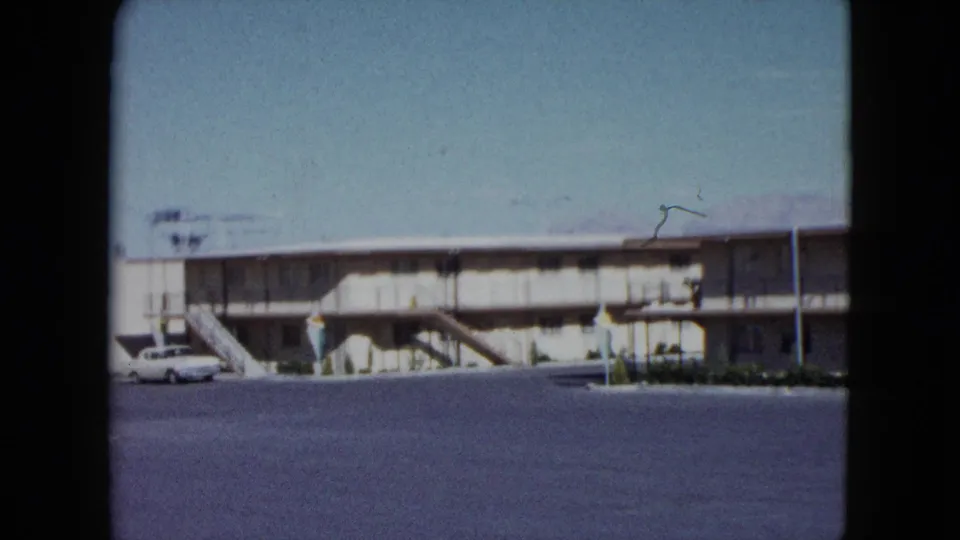 1959 Nevada motel view with exterior stairs, open parking lot, and a light-colored vintage car near the left side.