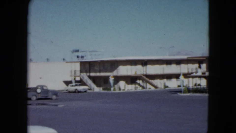 Final 1959 Nevada frame showing the motel facade, exterior stairs, open lot, and vintage cars near the lower edge.
