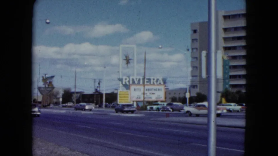A Nevada street view shows the Riviera sign, passing cars, and tall hotel buildings under a blue sky.