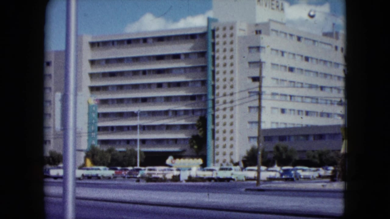 Riviera hotel exterior behind a roadway with parked and passing cars.