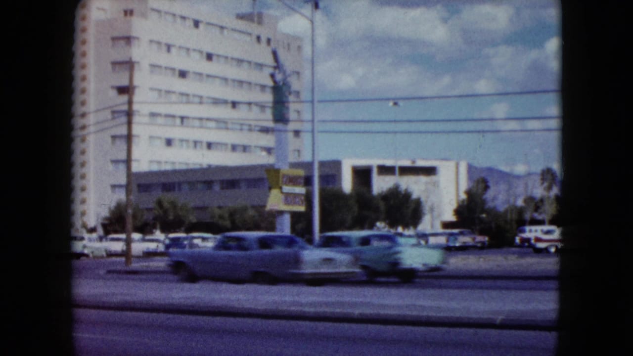 Cars pass in front of a modern building with utility wires across the frame.