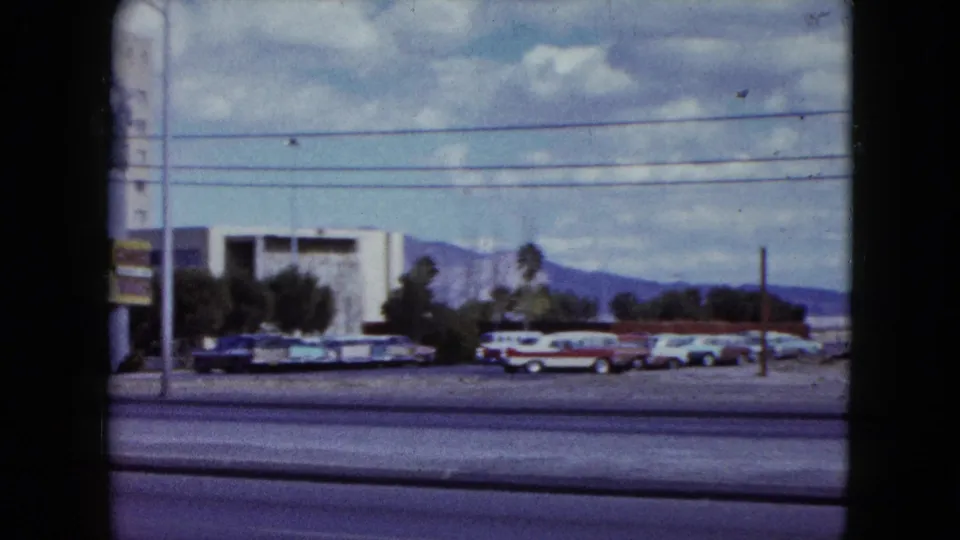 The pan settles on parked cars and a low modern building, with utility lines overhead and Nevada mountains visible in the distance.