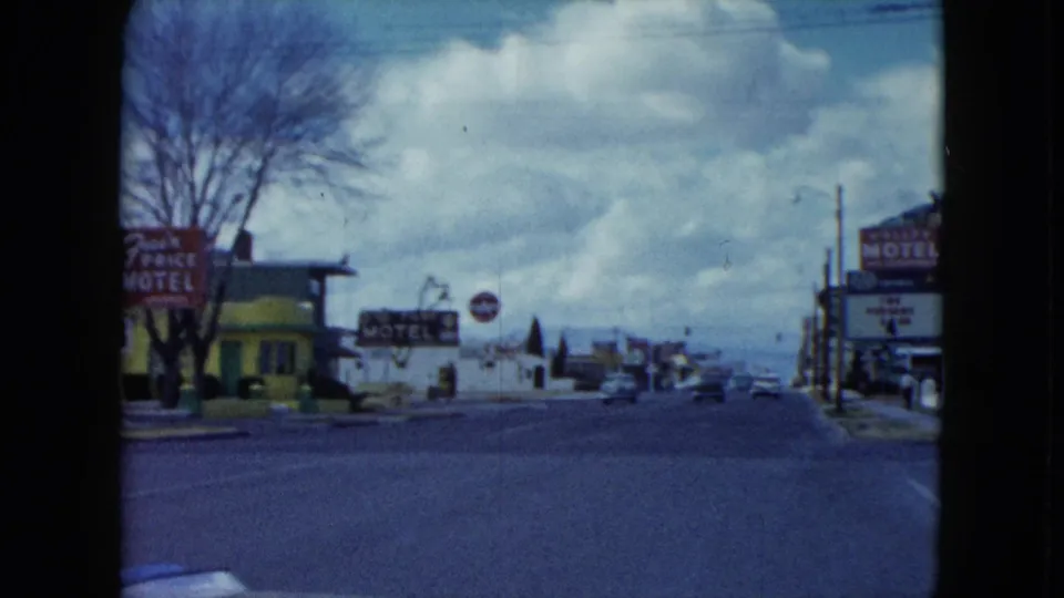1959 Nevada street view with motel signage, low commercial buildings, utility poles, cloudy sky, and distant mountain backdrop.